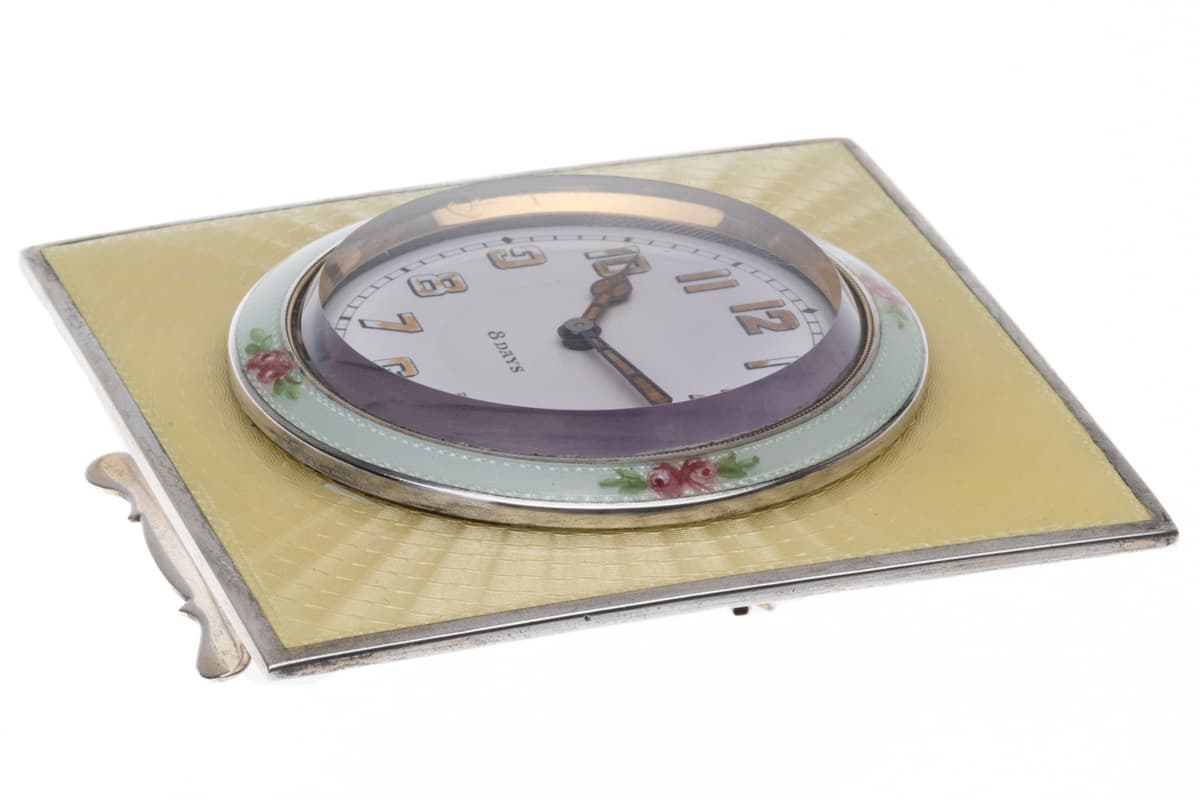 Low-angle view highlighting the domed crystal, white dial with gilt numerals, and hand-painted rose garlands on the silver bezel.